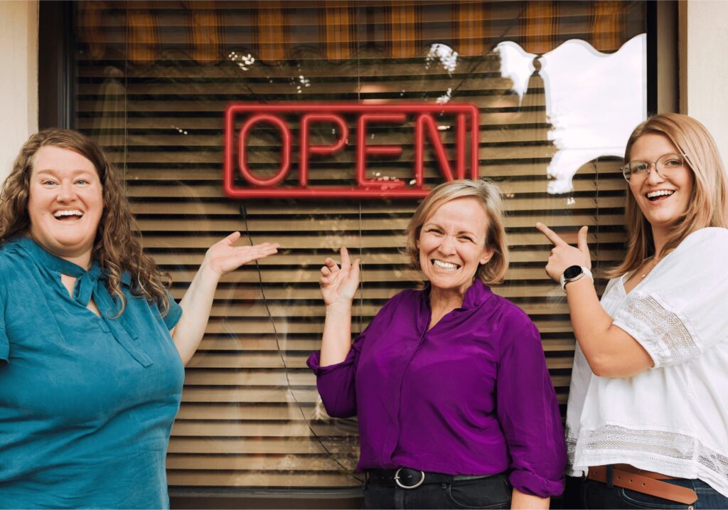 Lofgreen Marketing Team standing in front of an open sign at a small business store front.