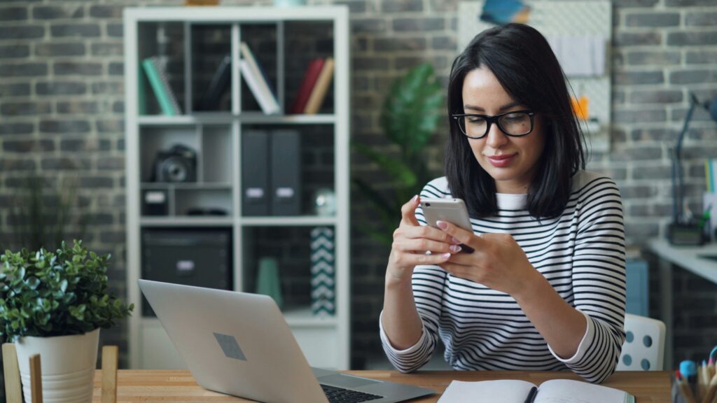 Woman on phone in front of laptop at desk